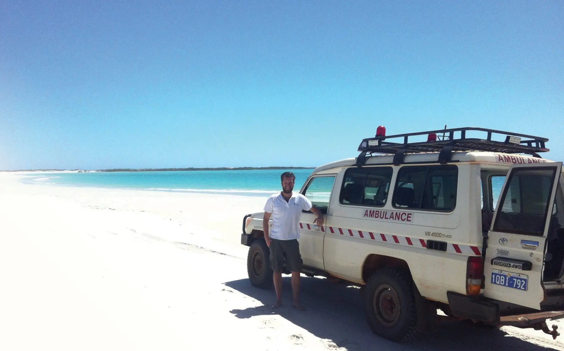Rory standing on a beach, leaning against a 4wd ambulance.