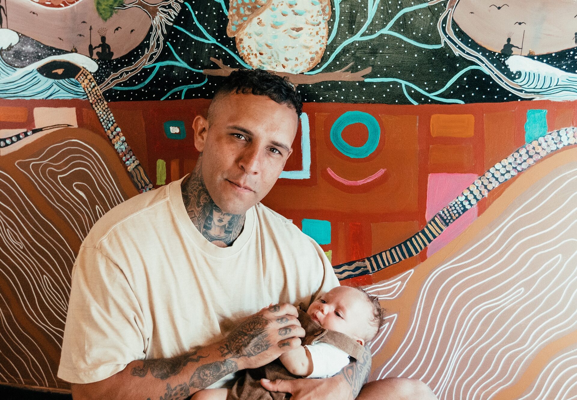 Man holding baby in front of mural.