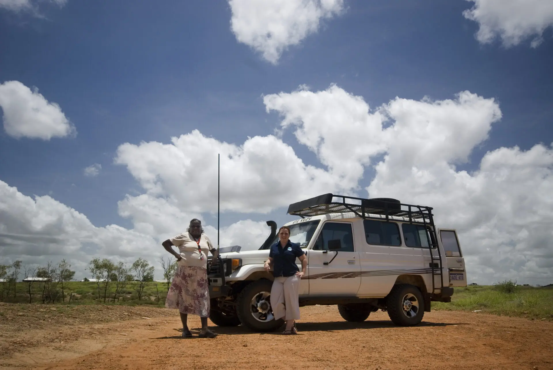 Two people leaning against a FWD on a dirt road