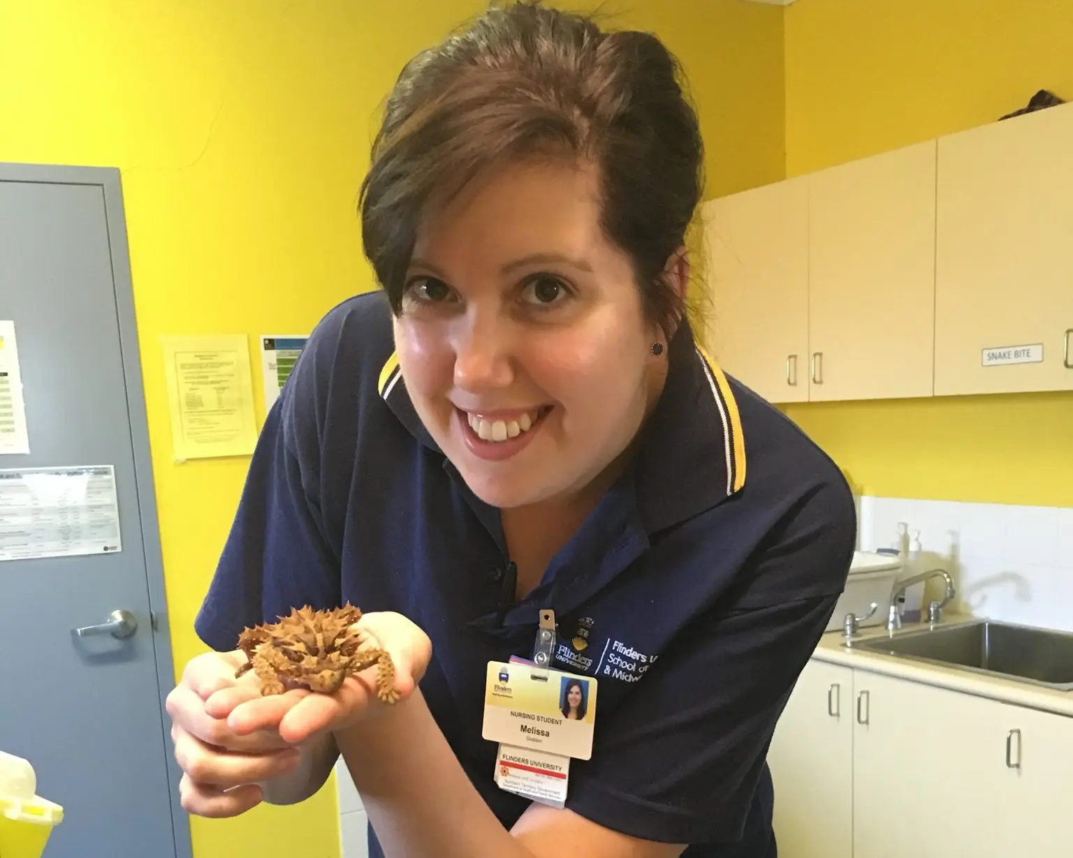Melissa smiling in a Flinders University polo shirt, holding a spiky lizard.