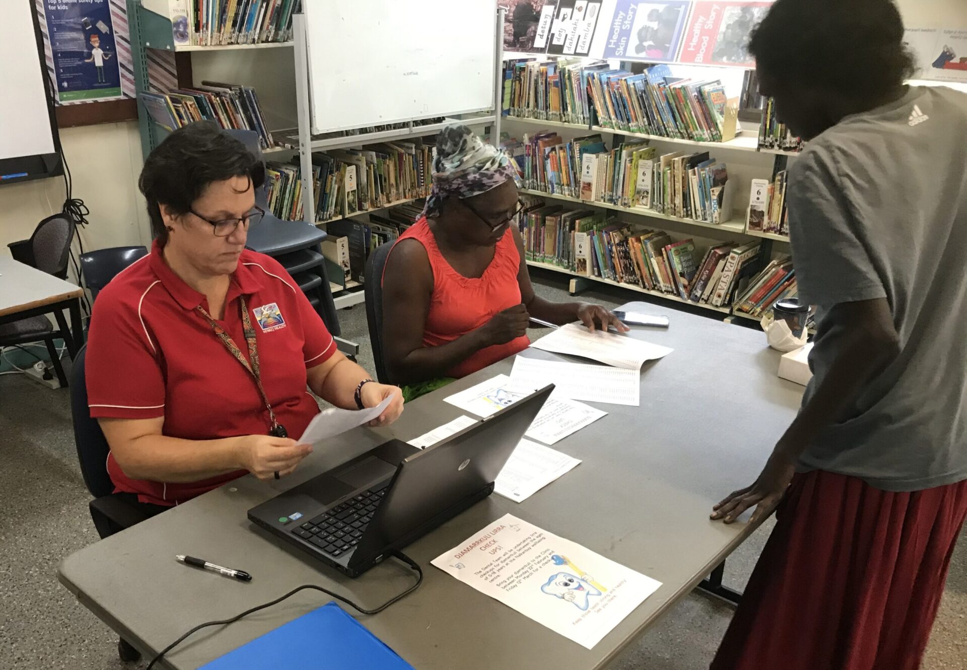 Kellie and an AHP in the school library cross-checking  new enrolments onto the clinical database.