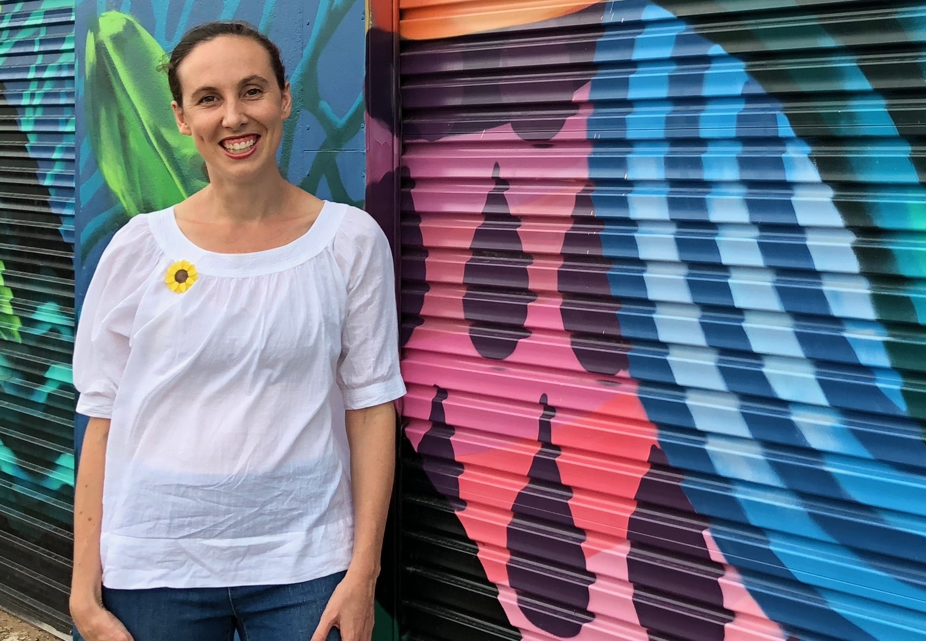 Woman standing and smiling infront of a colourful mural