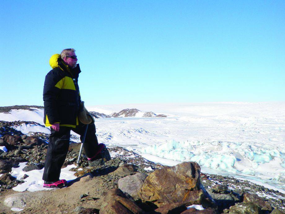 Person in snow gear standing at the top of a snowy mountain.