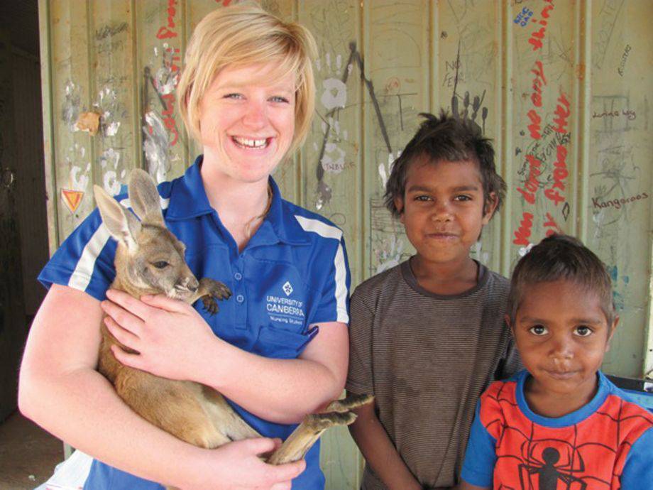 Person holding a baby kangaroo, two children standing next to them.