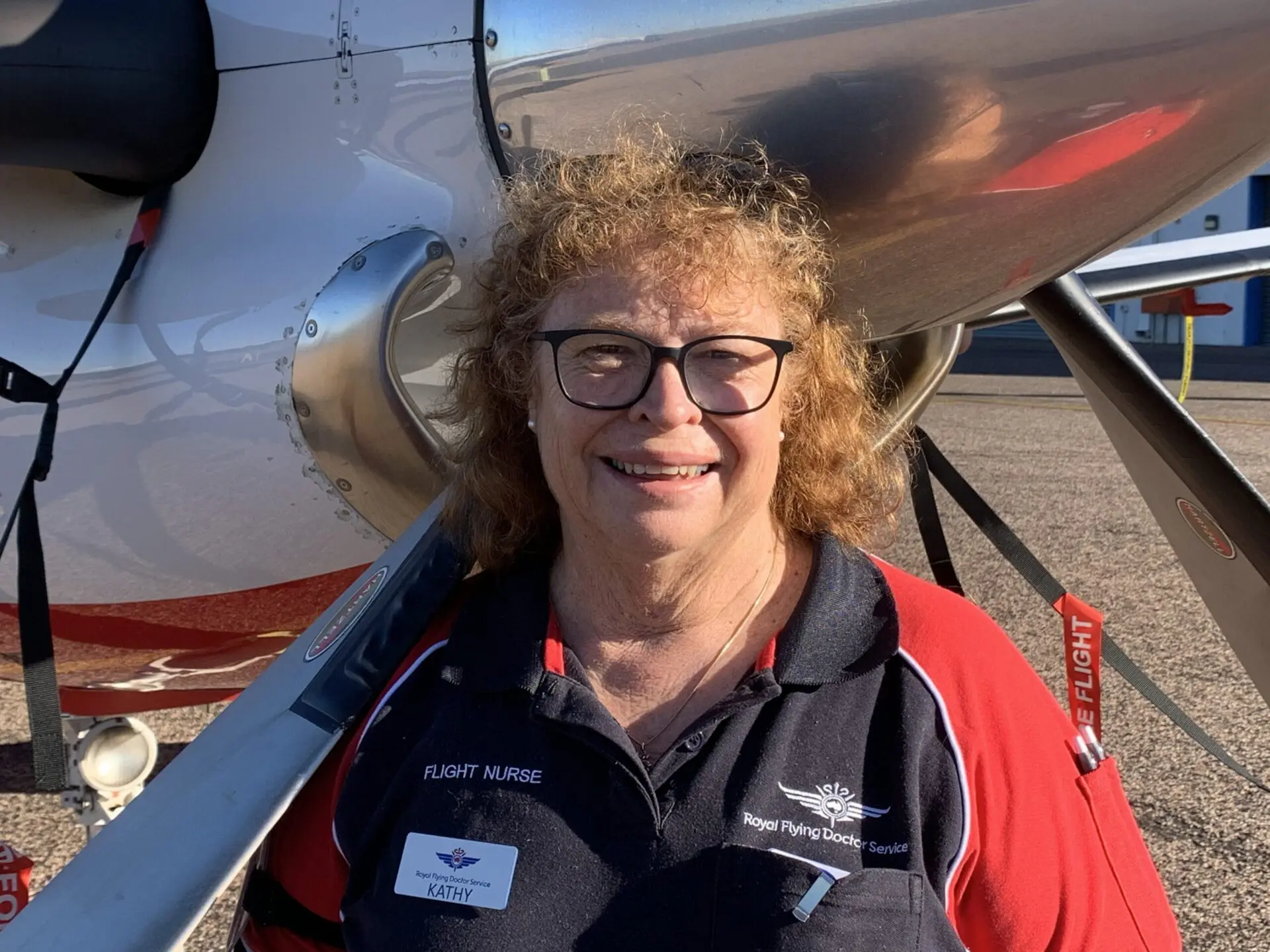 Kathy in an RFDS polo shirt, stood in front of an RFDS aircraft.