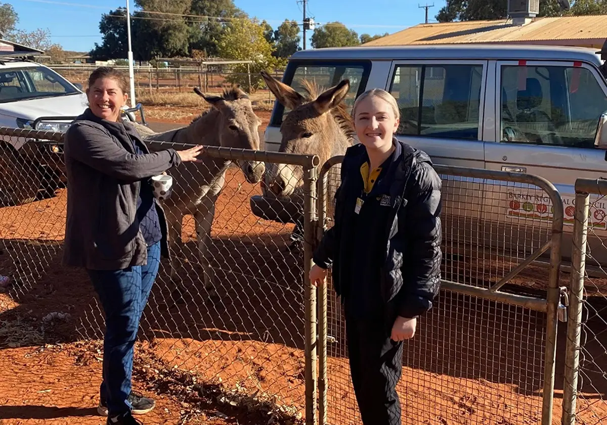 Jordyn and Kylie petting donkeys behind a wire fence.