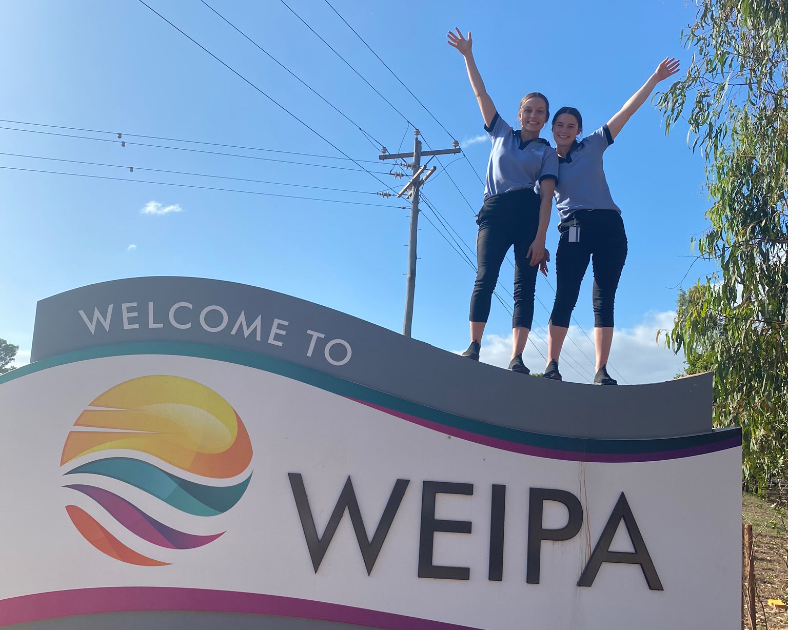 Natasha and colleague standing on a sign that reads 'Welcome to Weipa'.