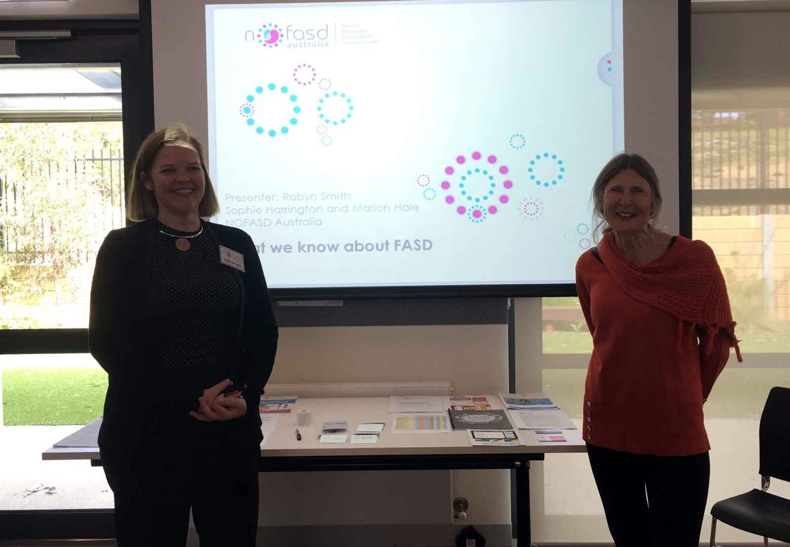 Two women standing in front of a projector screen presenting on FASD.