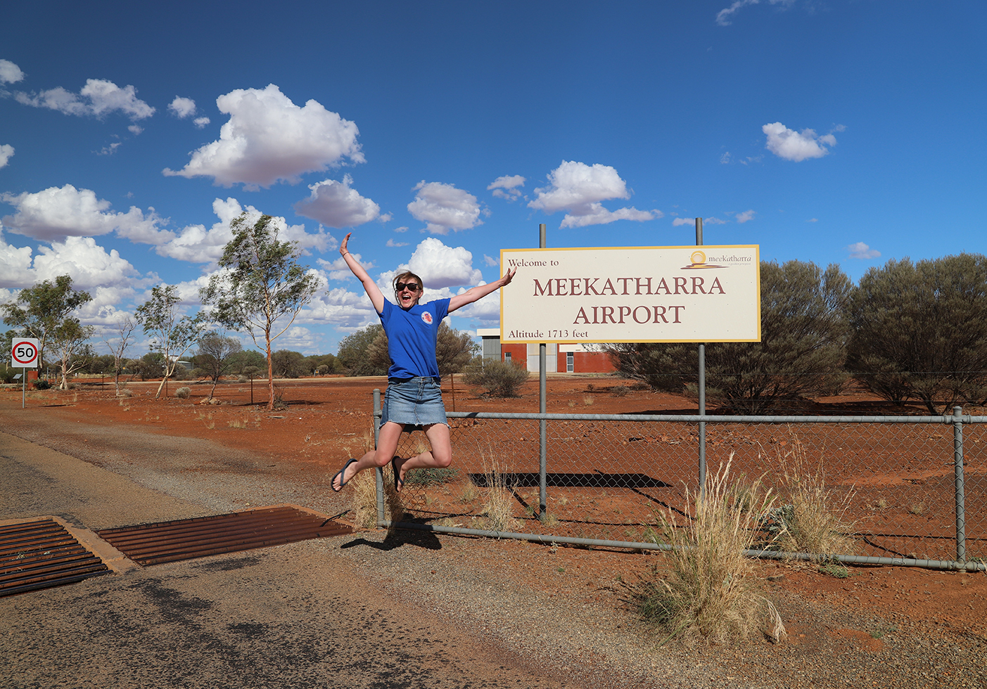 Sarah jumping for joy in front of Meekatharra Airport sign.