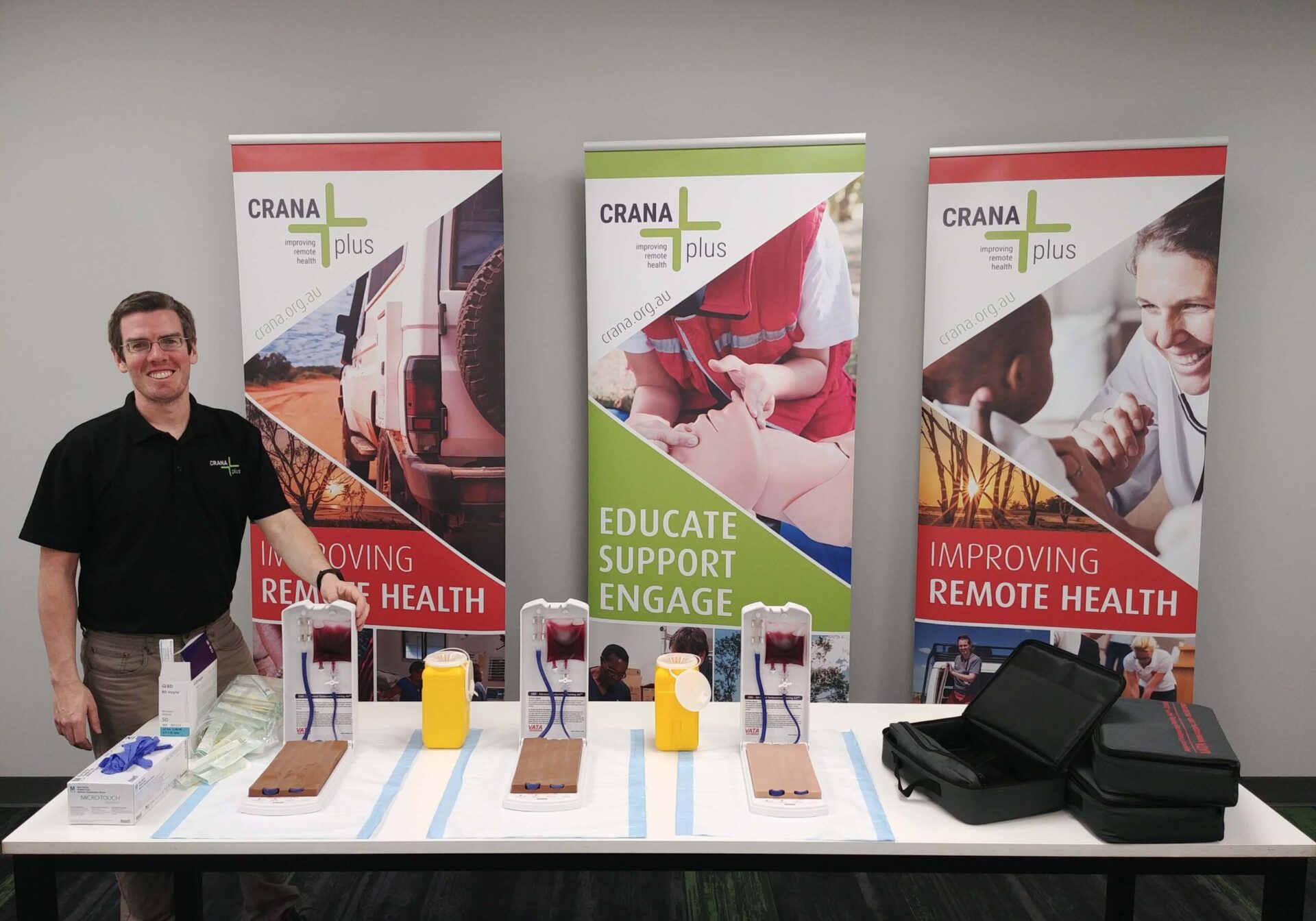 CRANAplus educator stood next to table with new equipment on display and CRANAplus banners in background.