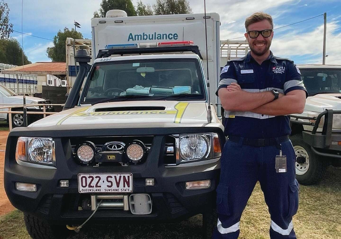Man standing with arms crossed, smiling, next to ambulance.